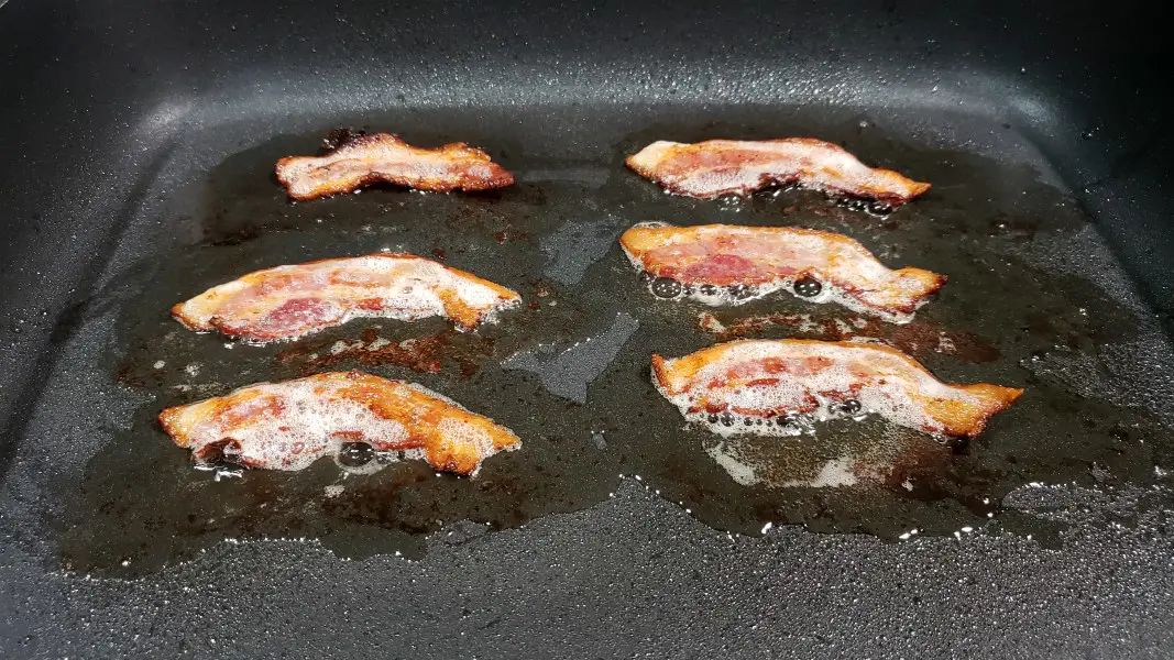 6 half slices of bacon cooking in an electric skillet