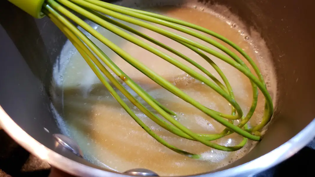 homemade sweetened condensed milk in a sauce pan with a whisk.