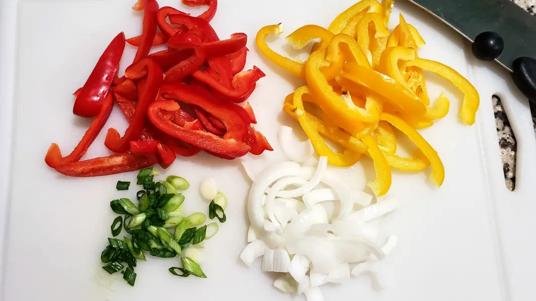 red bell pepper, yellow bell pepper, green onion, and white onion sliced on a cutting board.