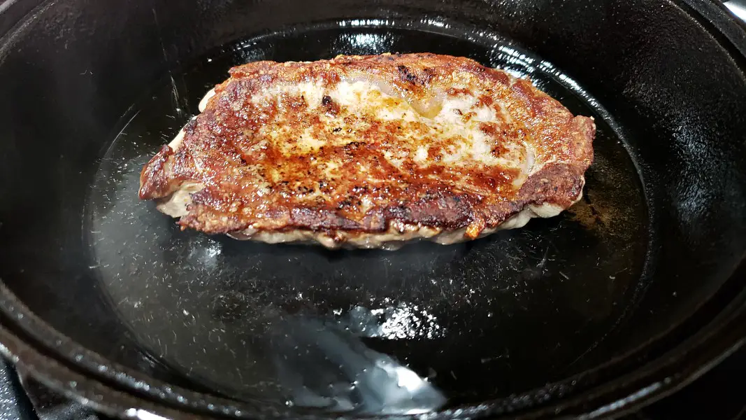 ribeye steak cooking in a cast iron skillet.