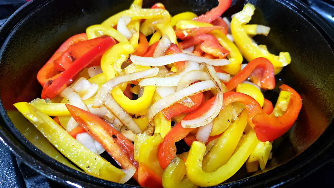 bell peppers and onions cooking in a cast iron skillet.