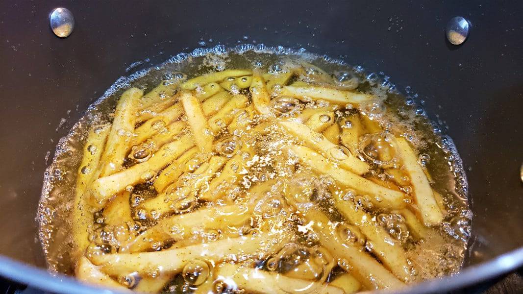 seasoned french fries deep frying in a pan.