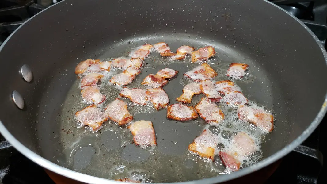 bacon pieces frying in a large pan.