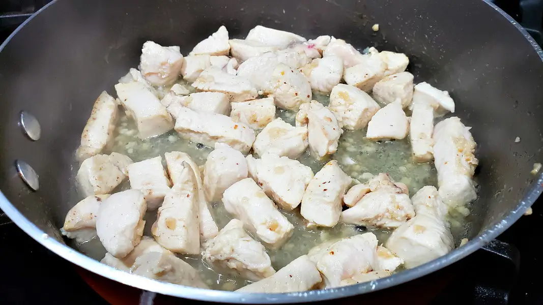 diced chicken and garlic cooking in a large pan.