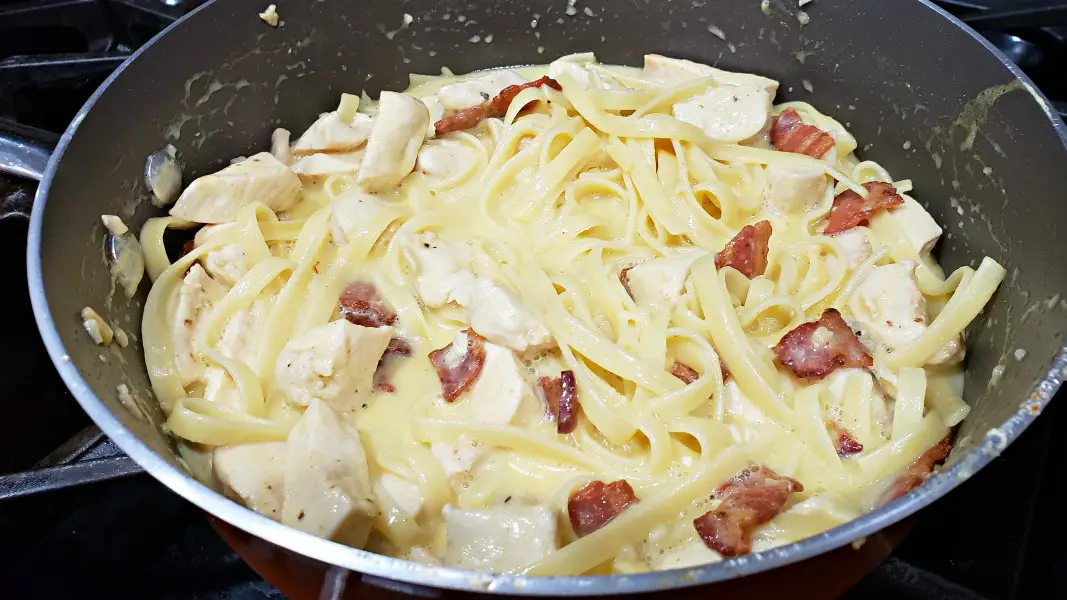 diced chicken, pasta, bacon, and parmesan sauce cooking in a large pan for this Chicken Carbonara recipe.
