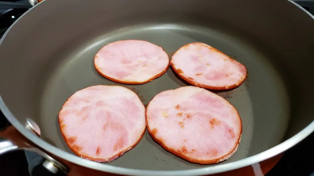four slices of Canadian bacon cooking in a pan.