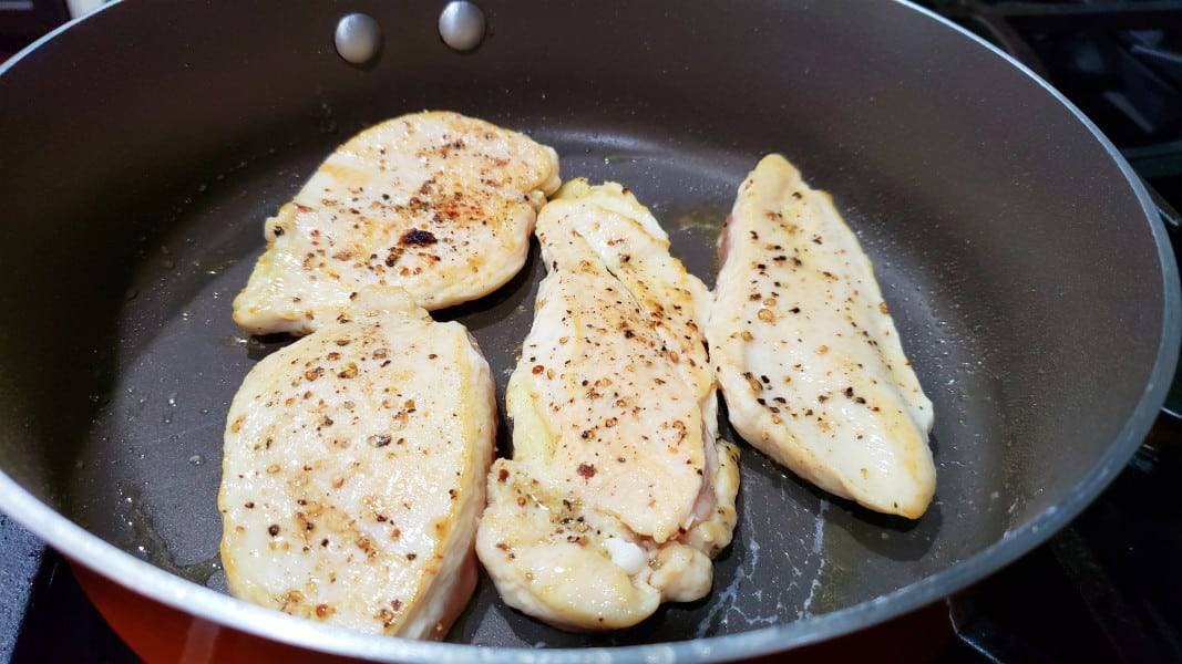 four pieces of boneless chicken cooking a pan.