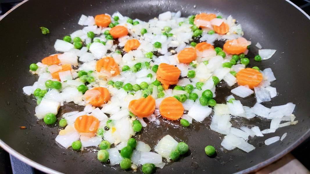 peas, carrots, onions, and garlic frying in a pan.