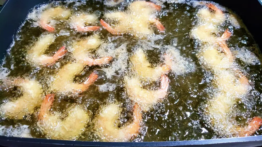 beer battered coconut shrimp deep frying in a pan.