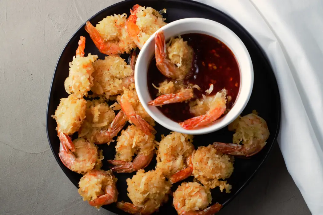 Fried Beer Battered Coconut Shrimp on a plate with a bowl of dipping sauce.