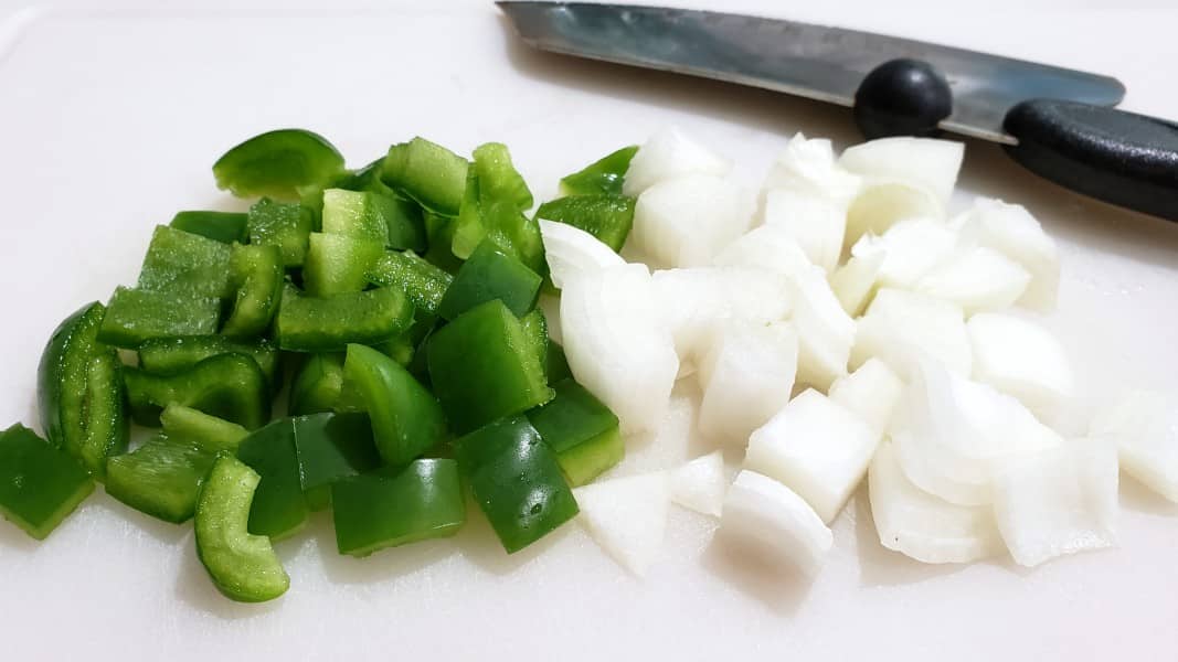 diced green pepper and diced onion on a cutting board with a knife.