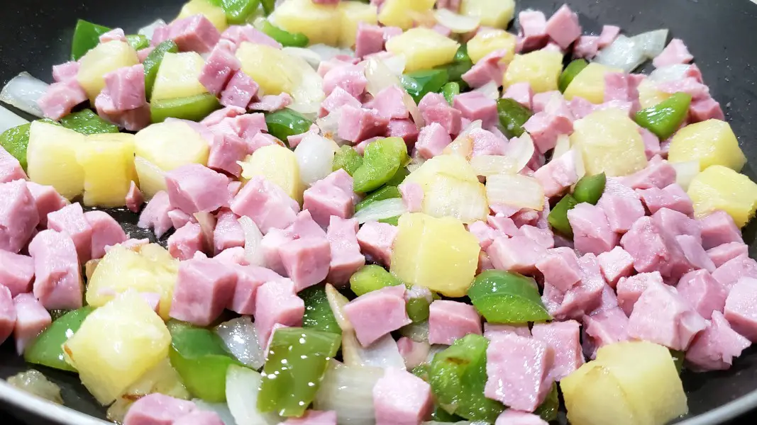 ham, pineapple, green pepper, and onion cooking in a pan.