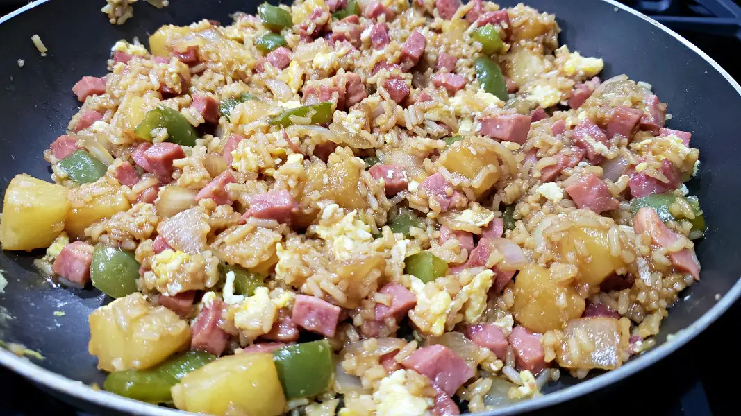 Hawaiian fried rice with ham and pineapple cooking in a pan.