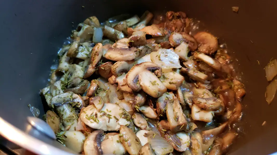 mushrooms, onions, and thyme cooking in a saucepan.