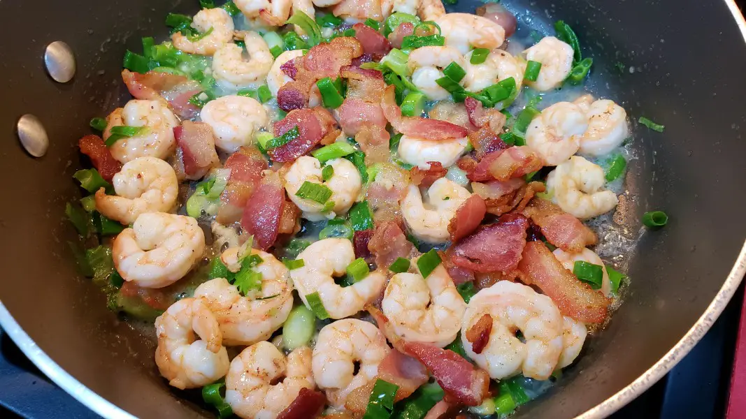 shrimp, bacon, garlic, and green onion frying in a pan.