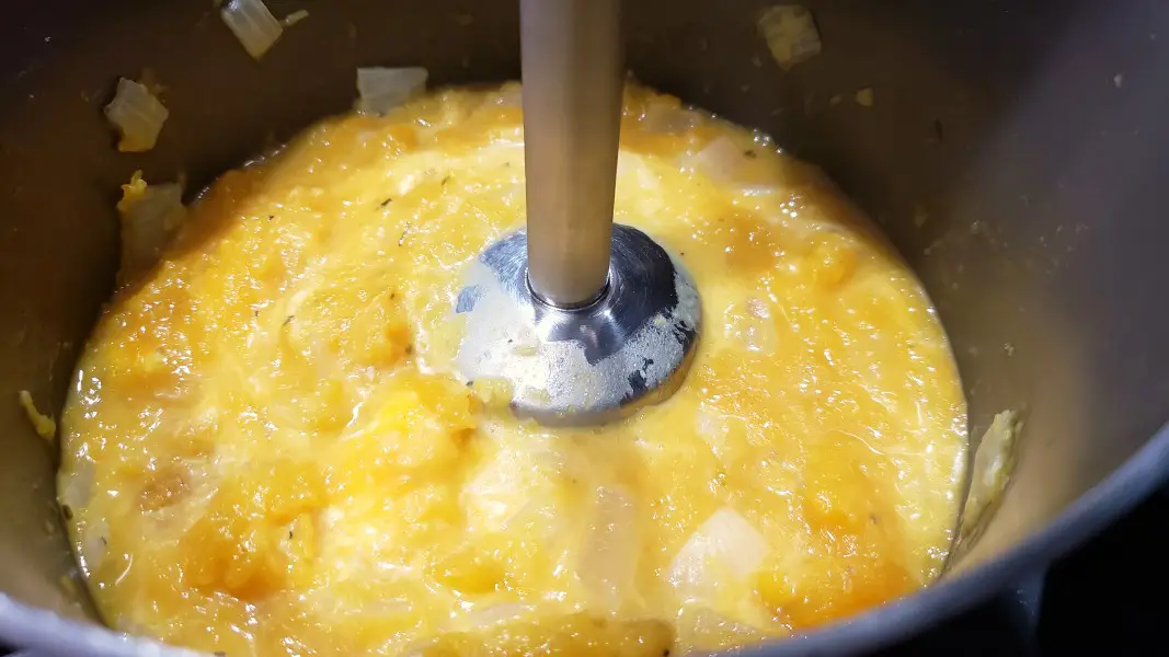 in immersion blender blending cream cheese into butternut squash soup.