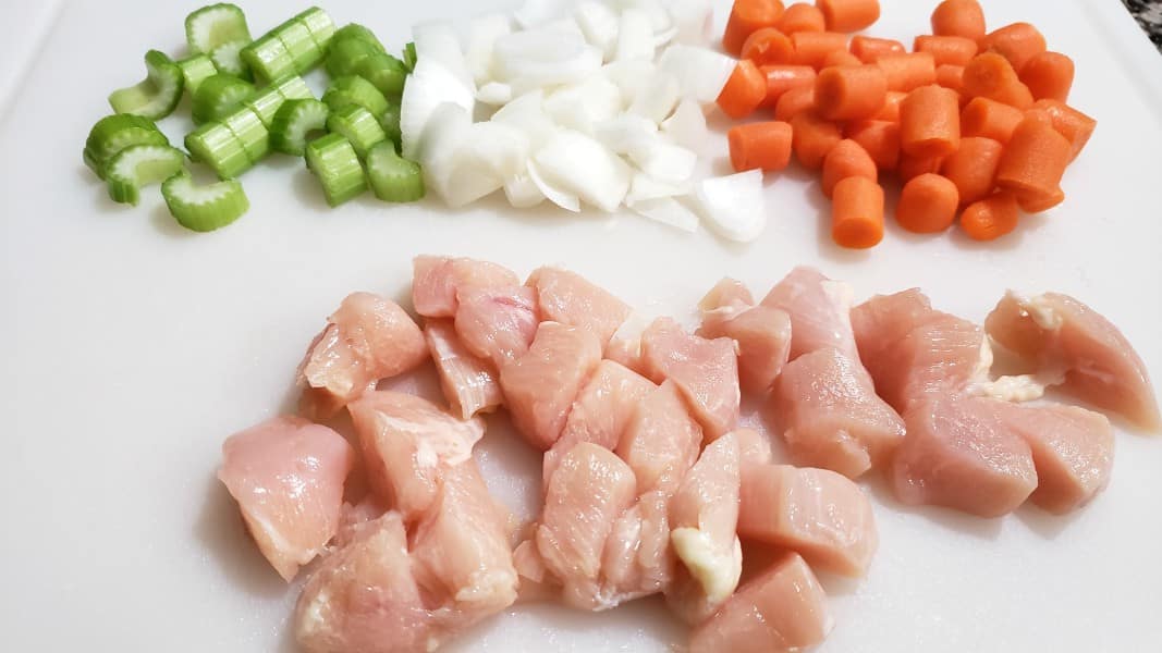 diced celery, onion, carrots, and chicken on a cutting board.