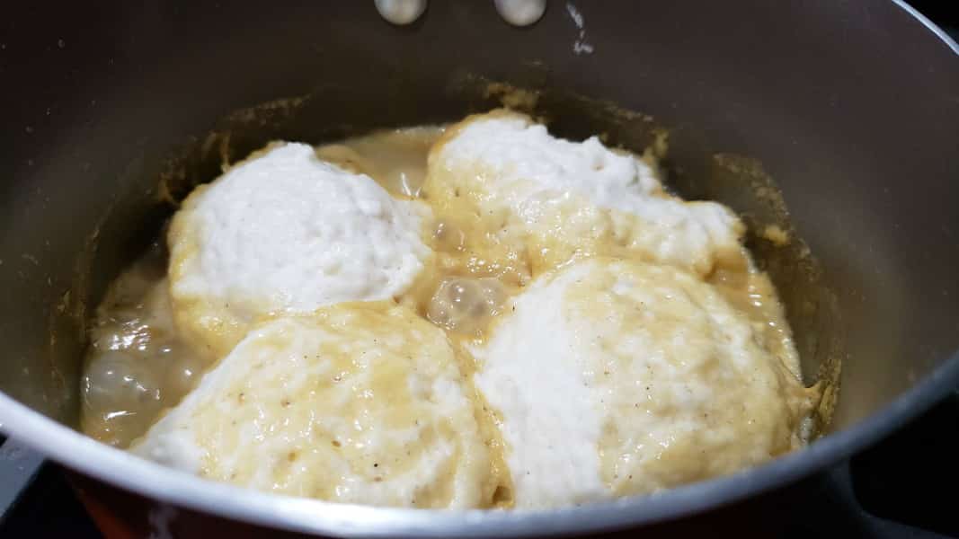 chicken stew and fluffy dumplings cooking in a pan.