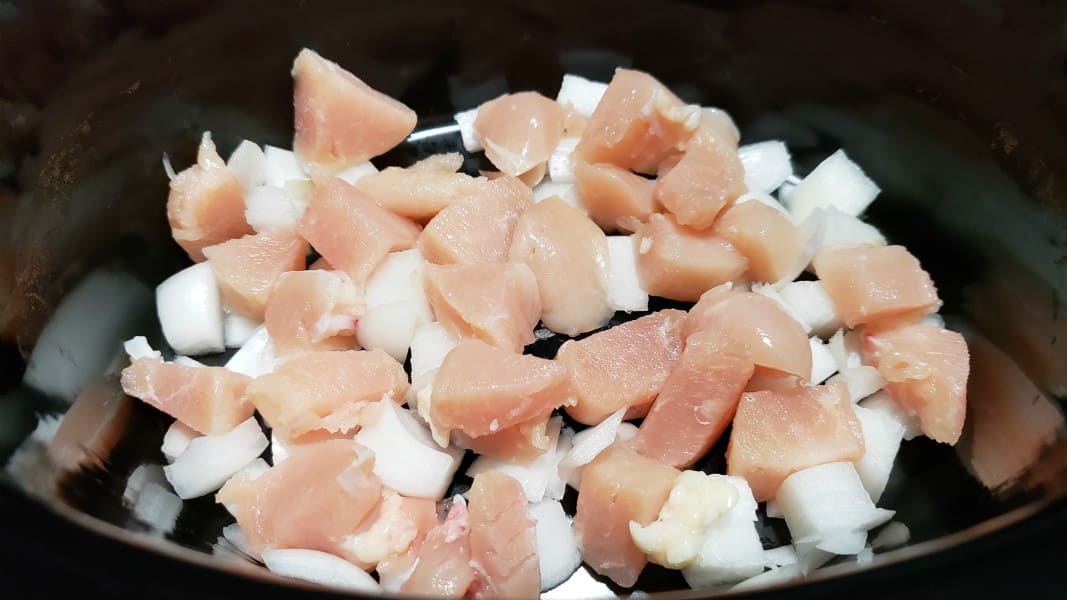 diced onions and chicken in a slow cooker crock pot.