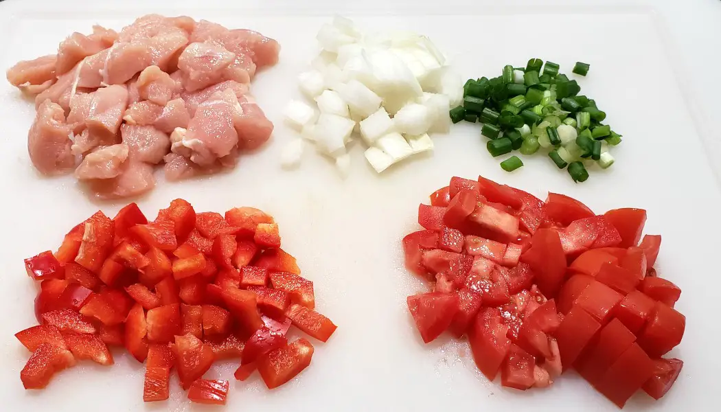 diced chicken, onion, green onion, red bell pepper, and roma tomato on a cutting board