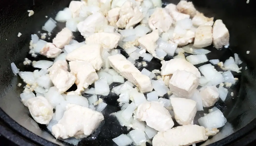 diced chicken, onion, and garlic cooking in a skillet