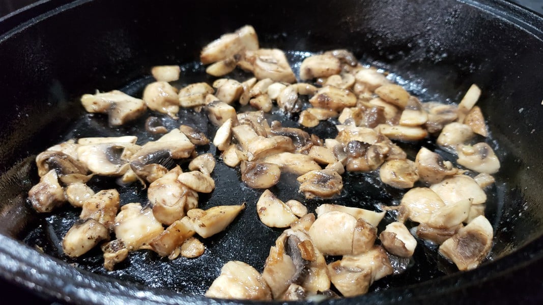 chopped mushrooms cooking in a cast iron skillet.