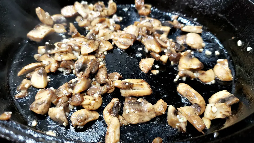 mushrooms, salt, pepper, and garlic cooking in a skillet.