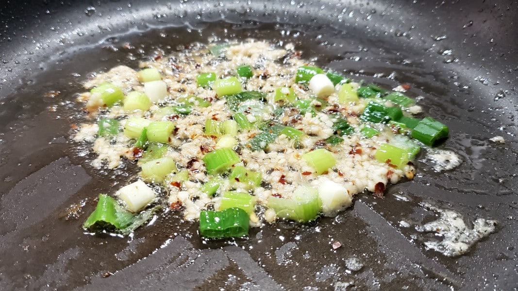 green onion, garlic and red pepper flakes cooking in a frying pan.