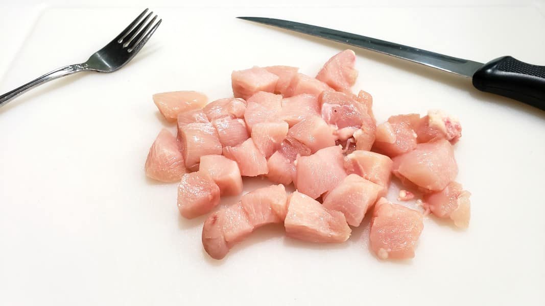 diced chicken on a cutting board with a fork and knife.
