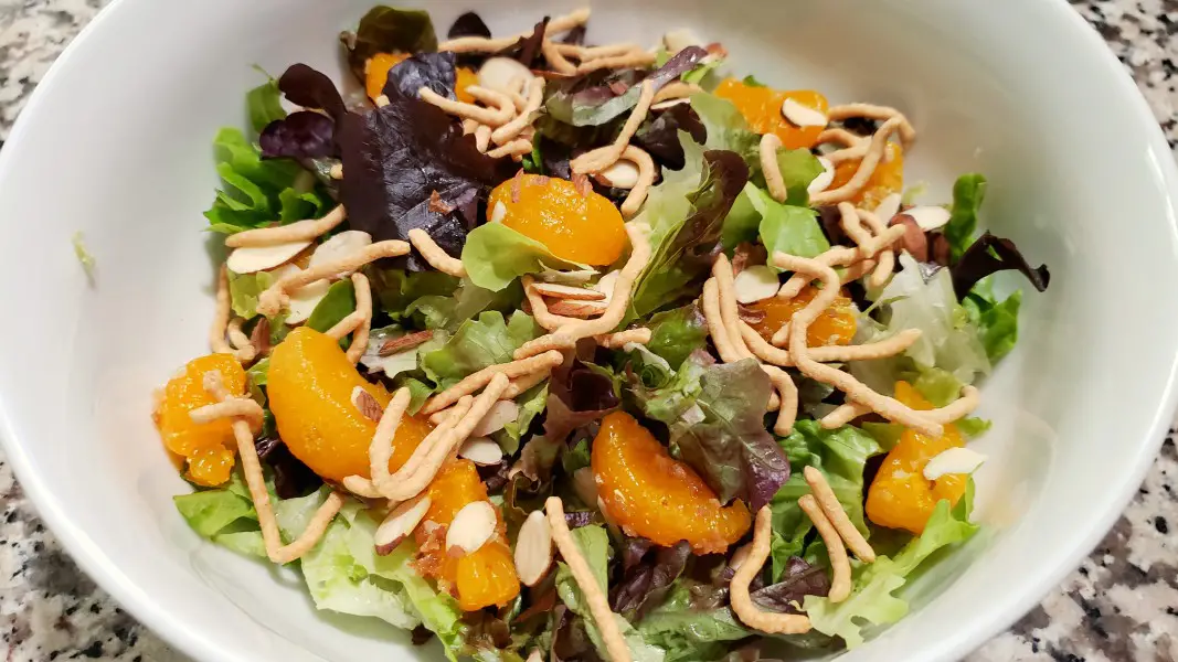 oriental salad with lettuce, almonds, chow mein noodles and mandarin oranges in a bowl.