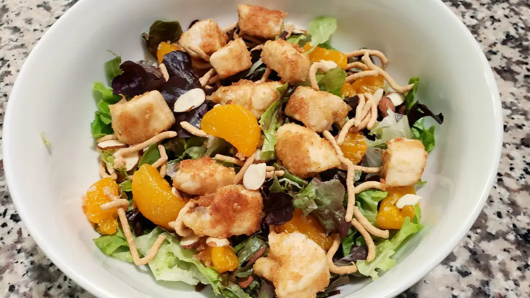chicken oriental salad with lettuce, almonds, chow mein noodles, chicken and mandarin oranges in a bowl.