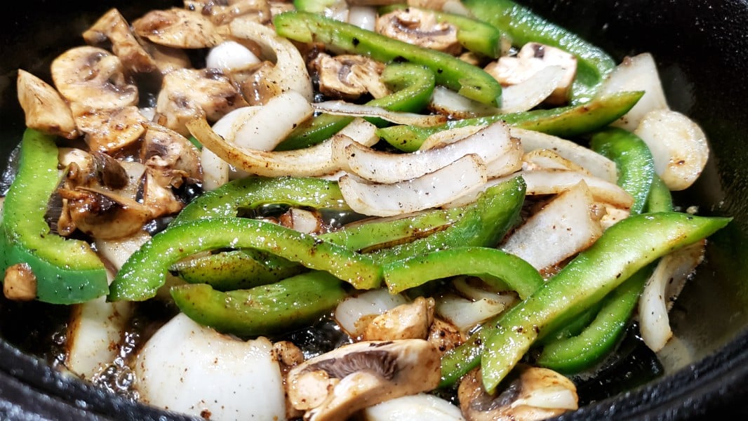 onions, mushrooms, and green pepper frying in a pan