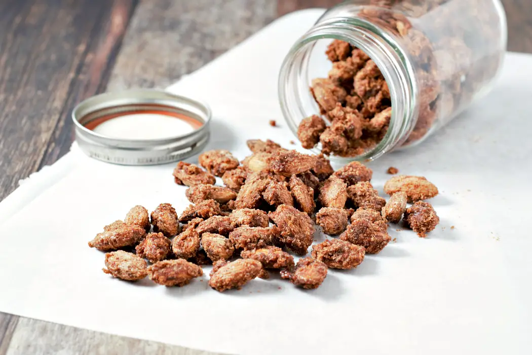 a Small Batch Candied Almonds spilling out of a jar.