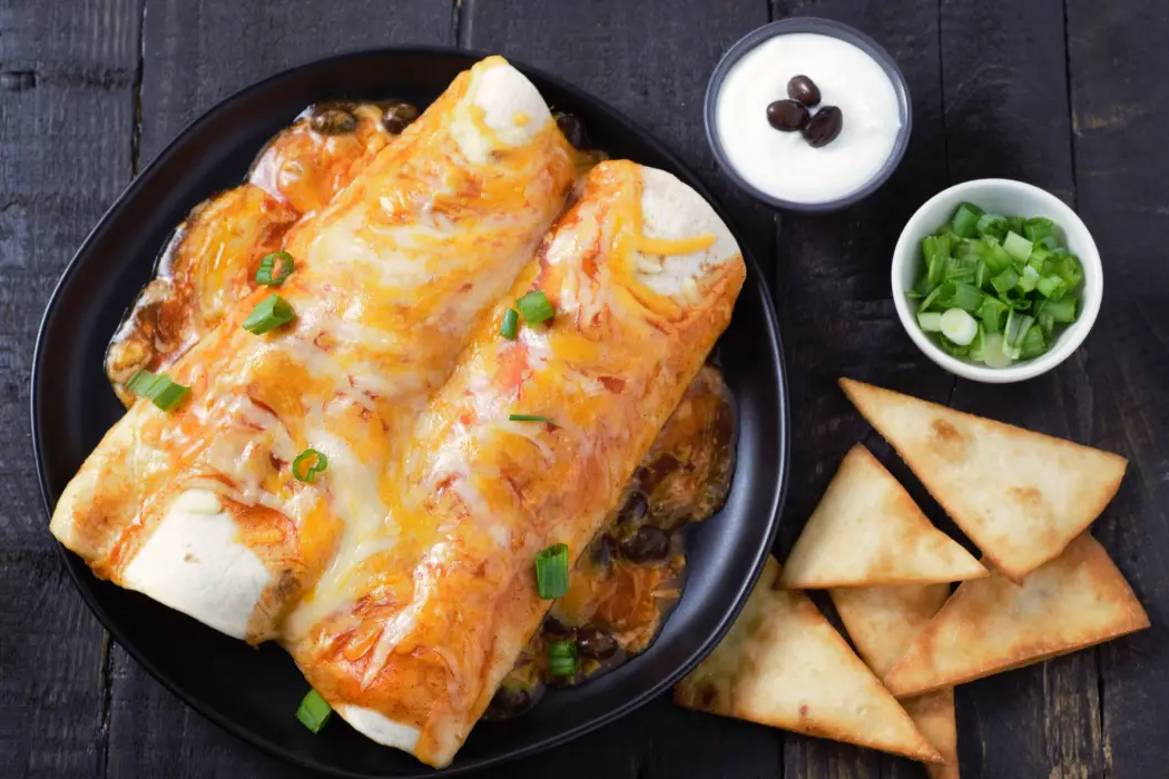 Chicken and Black Bean Enchiladas on a plate with sour cream and green onion