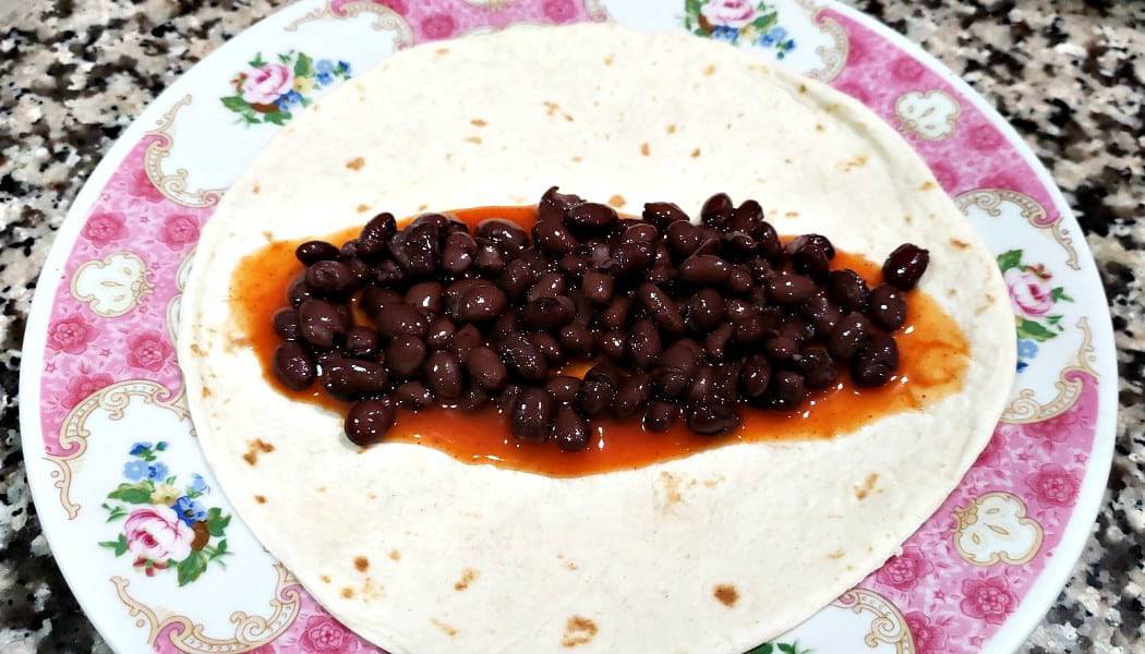 a plate with one tortilla topped with enchilada sauce and black beans