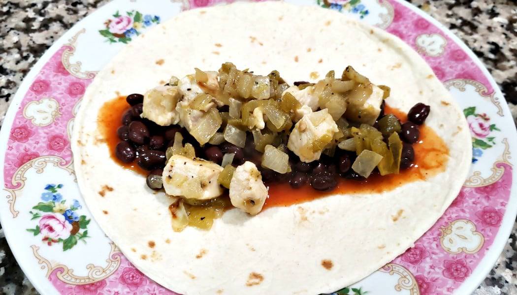 a plate with one tortilla topped with enchilada sauce, black beans, and chicken mixture