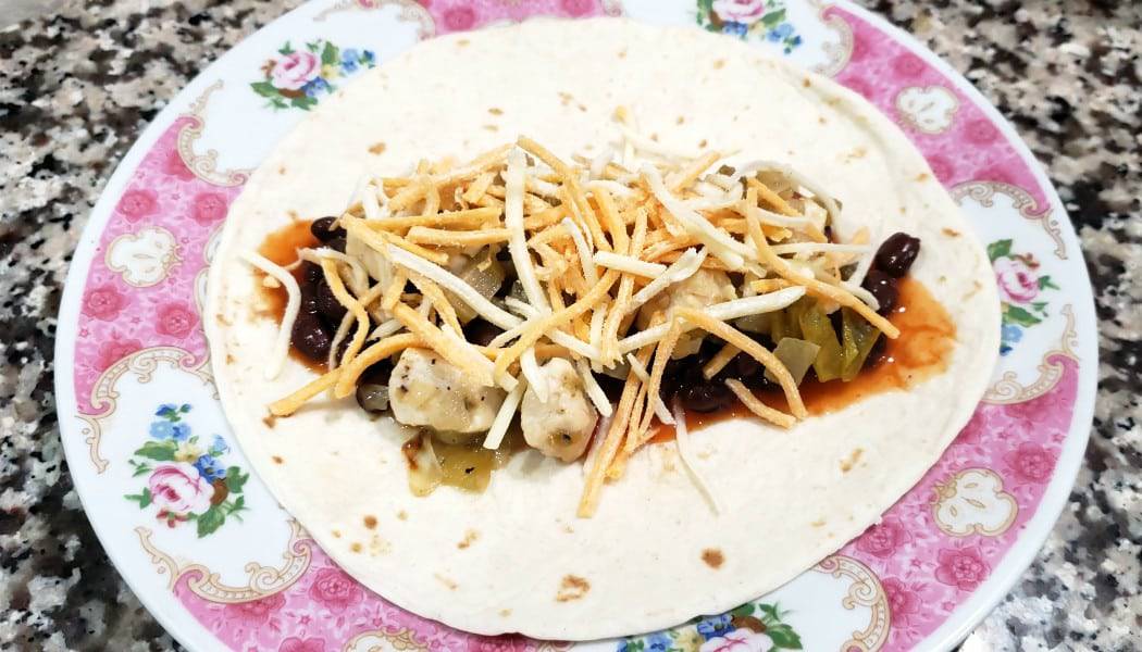 a tortilla topped with sauce, beans, chicken mixture, and cheese