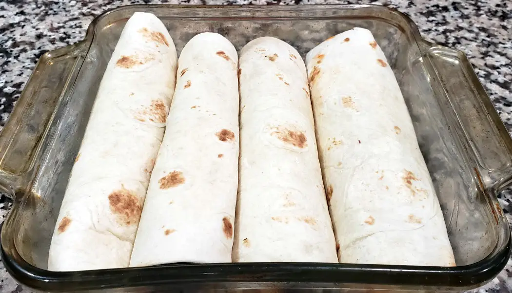 four chicken enchiladas rolled up in a baking dish