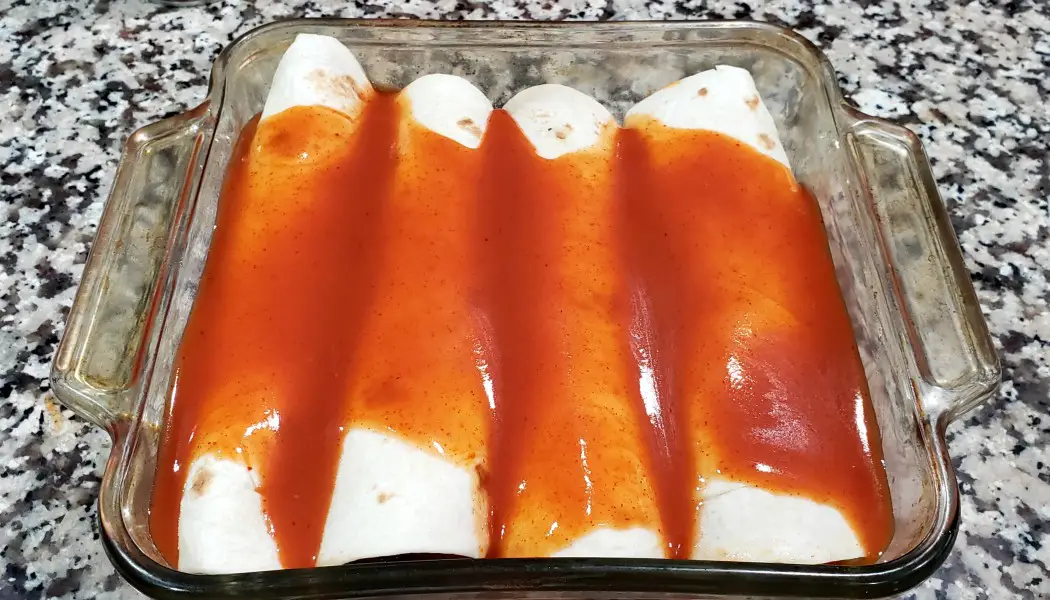 four chicken enchiladas rolled up in a baking dish topped with enchilada sauce