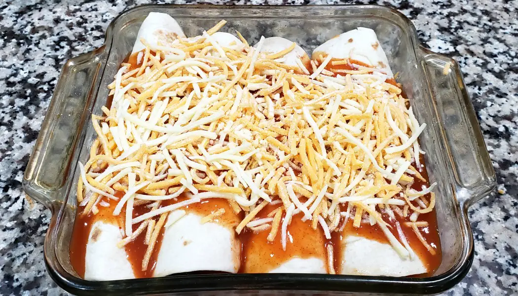 4 chicken enchiladas topped with sauce and cheese in a baking dish