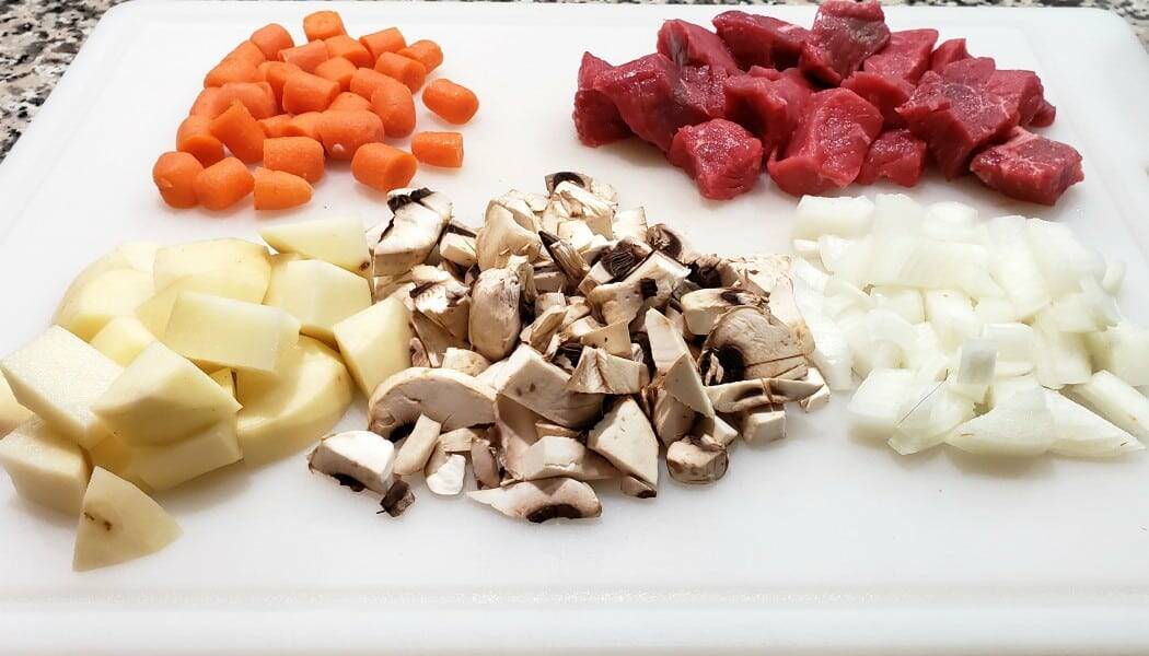 carrots, beef, potatoes, mushrooms, and onions chopped and diced on a cutting board
