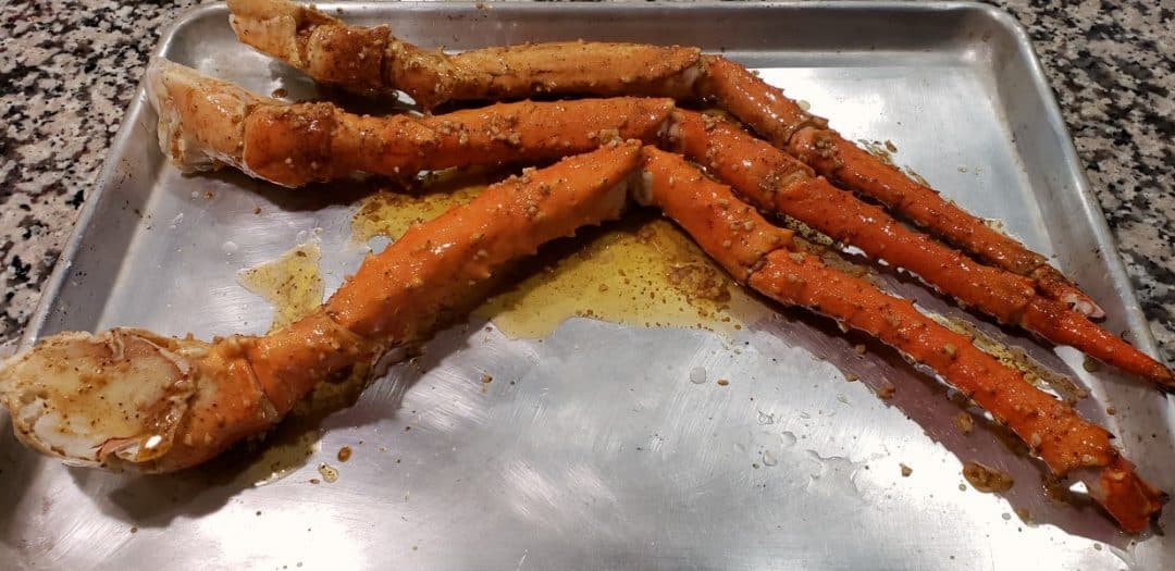 king crab legs brushed with butter mixture on a baking pan ready to bake