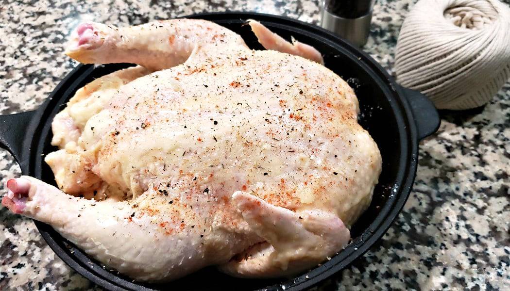 salt, pepper, thyme, and paprika sprinkled onto a whole chicken in a cast iron skillet.