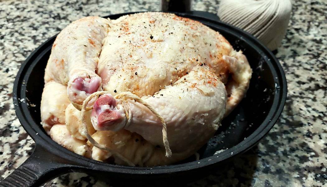 a whole chicken with the legs tied with kitchen cooking twine in a cast iron skillet ready to bake.