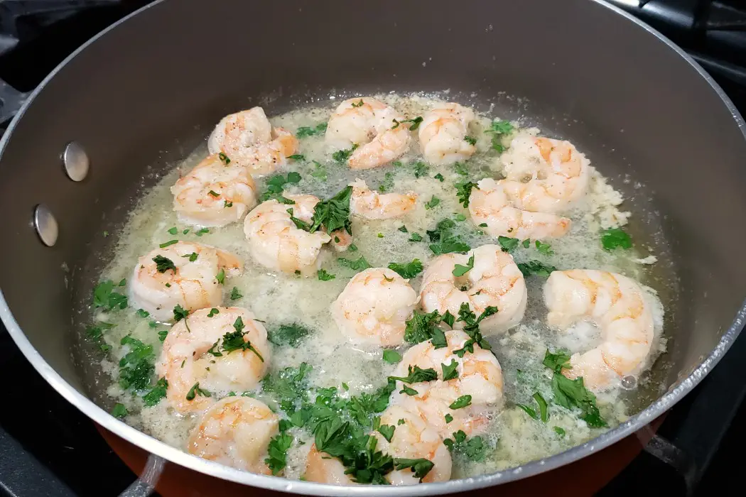 shrimp scampi frying in a pan with fresh parsley
