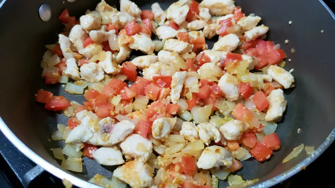 tomatoes, chicken, onion and garlic cooking in a pan