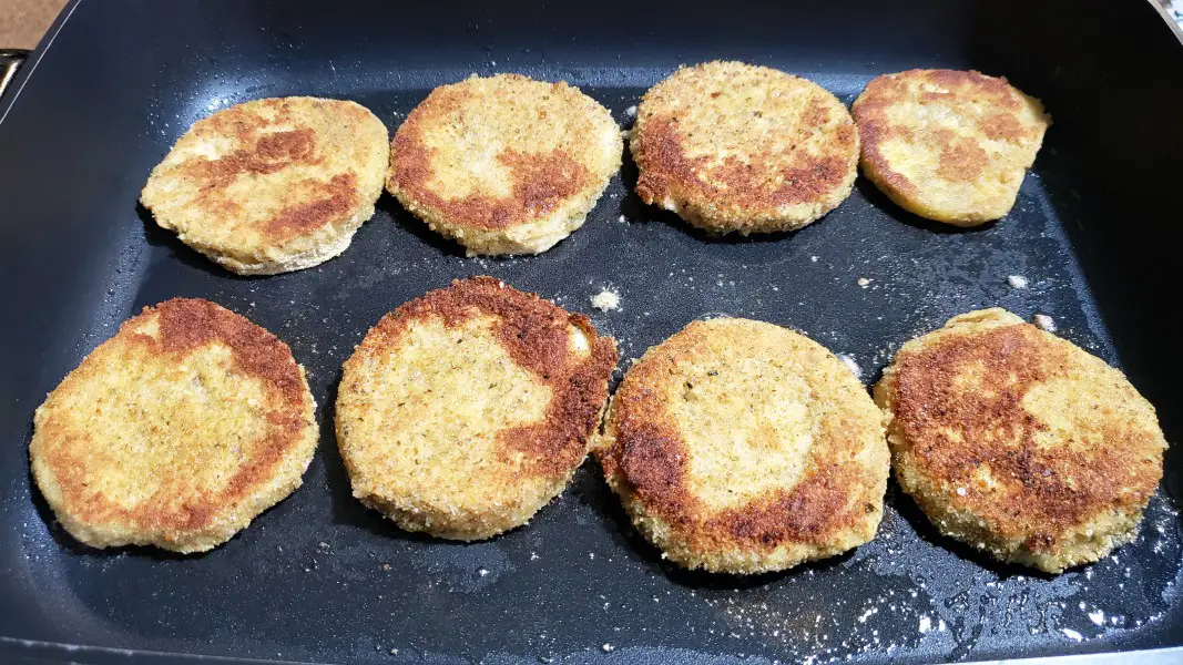 8 breaded eggplant slices frying in a skillet