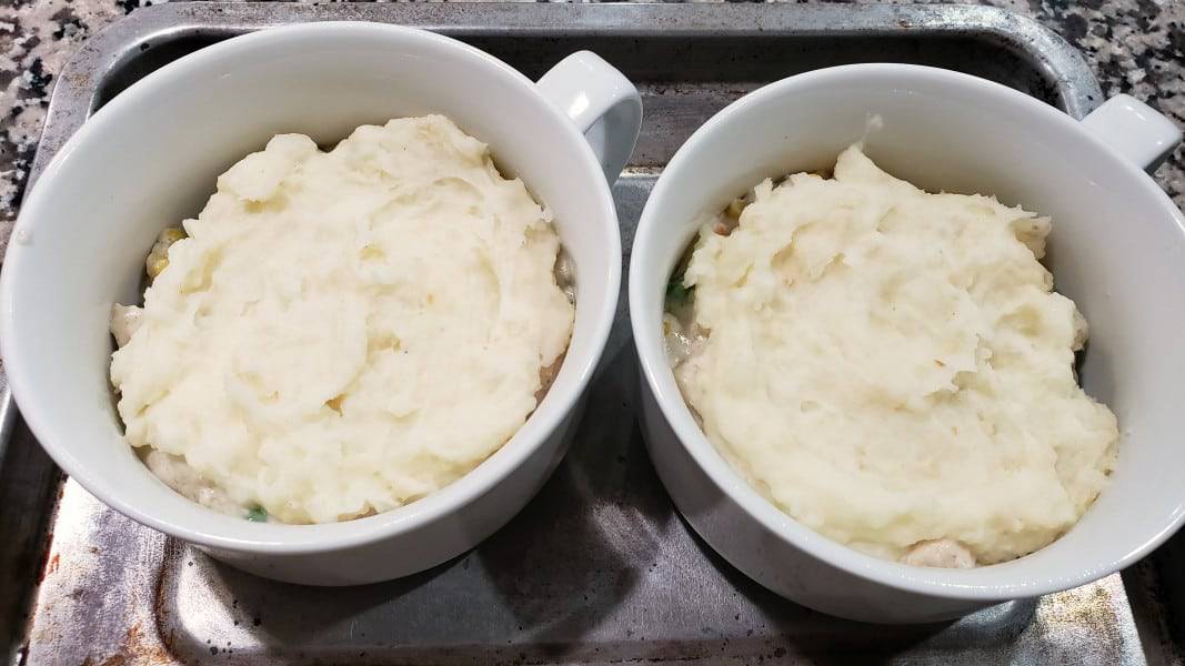 mashed potatoes on top of chicken cottage pie filling in two bowls