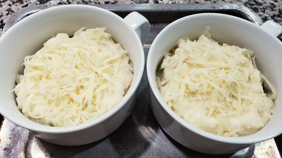 swiss cheese on top of mashed potatoes and chicken cottage pie filling in two bowls