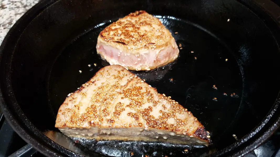 two sesame seed coated tuna steaks searing in a cast iron skillet